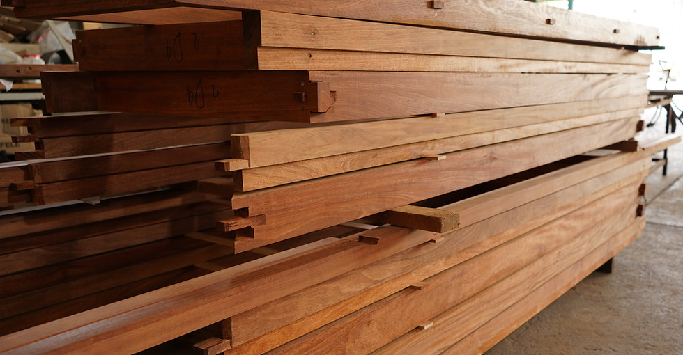 Stacks of high-quality raw solid timber planks with precise cut joints, being prepared for custom door frame fabrication at the THAVII woodworking factory in Samut Sakhon, Thailand.