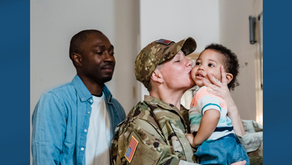 A military service person kissing a baby on the cheek while their partner looks on.
