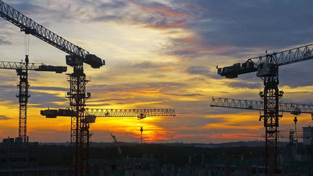 Multiple cranes at a construction site against a backdrop of a breathtaking sunset with dramatic clouds and light play