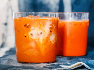 Two glasses of iced Thai tea with swirling cream on a blue cloth. The bright orange drink contrasts with the dark, blurred background.