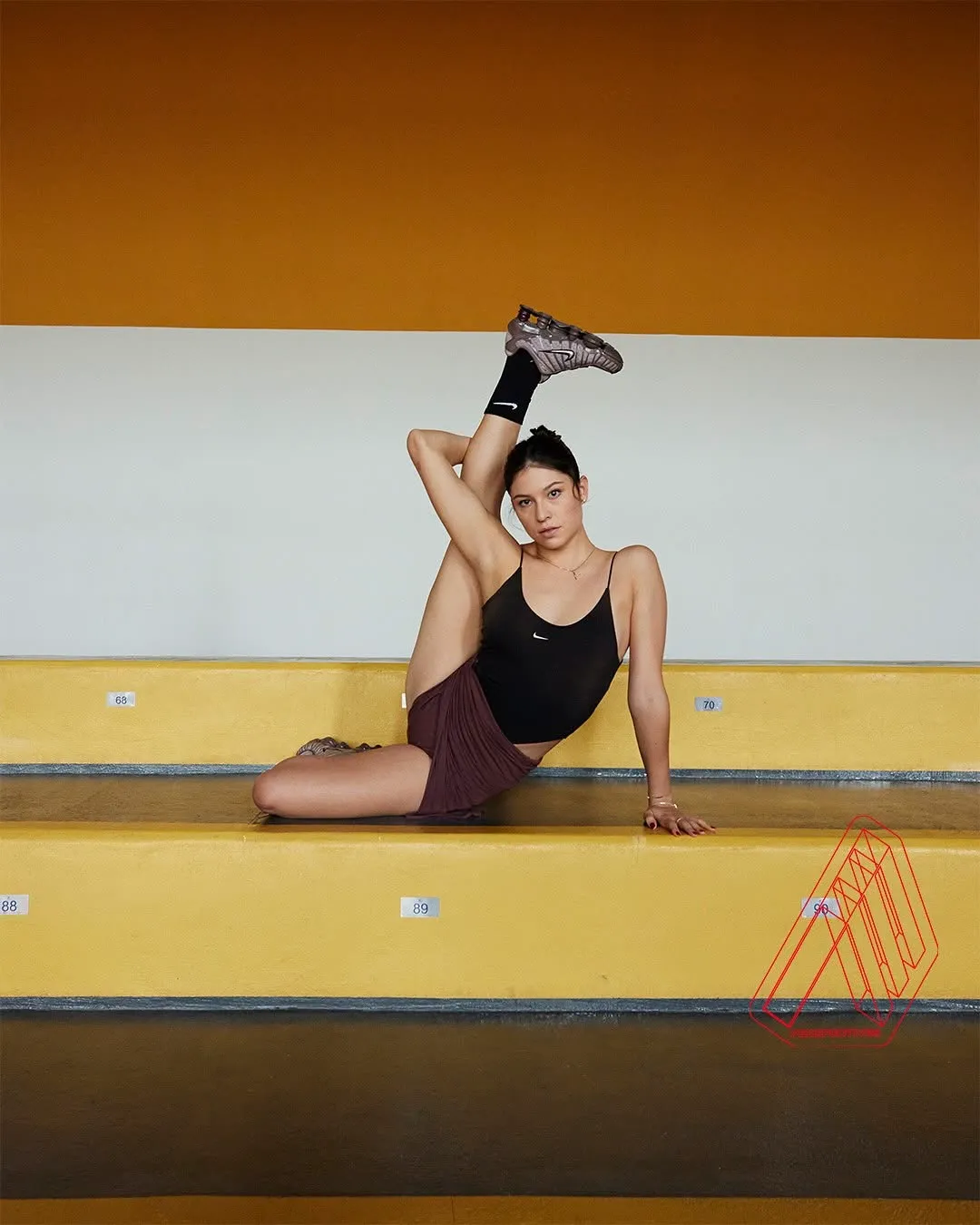 Woman stretches on yellow bleachers, leg extended, looking at the camera.