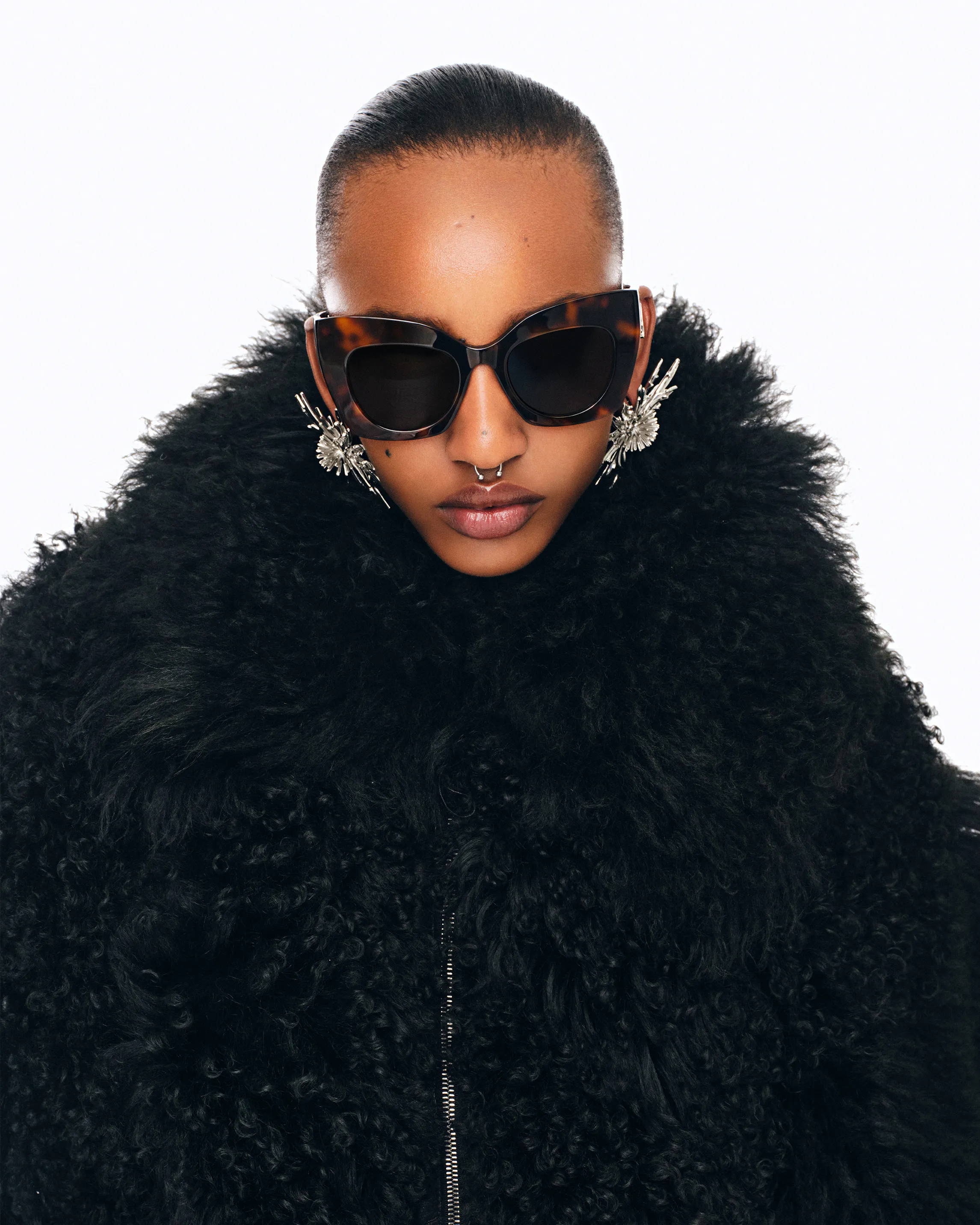 Woman wearing sunglasses and black fur coat, studio shot against white background
