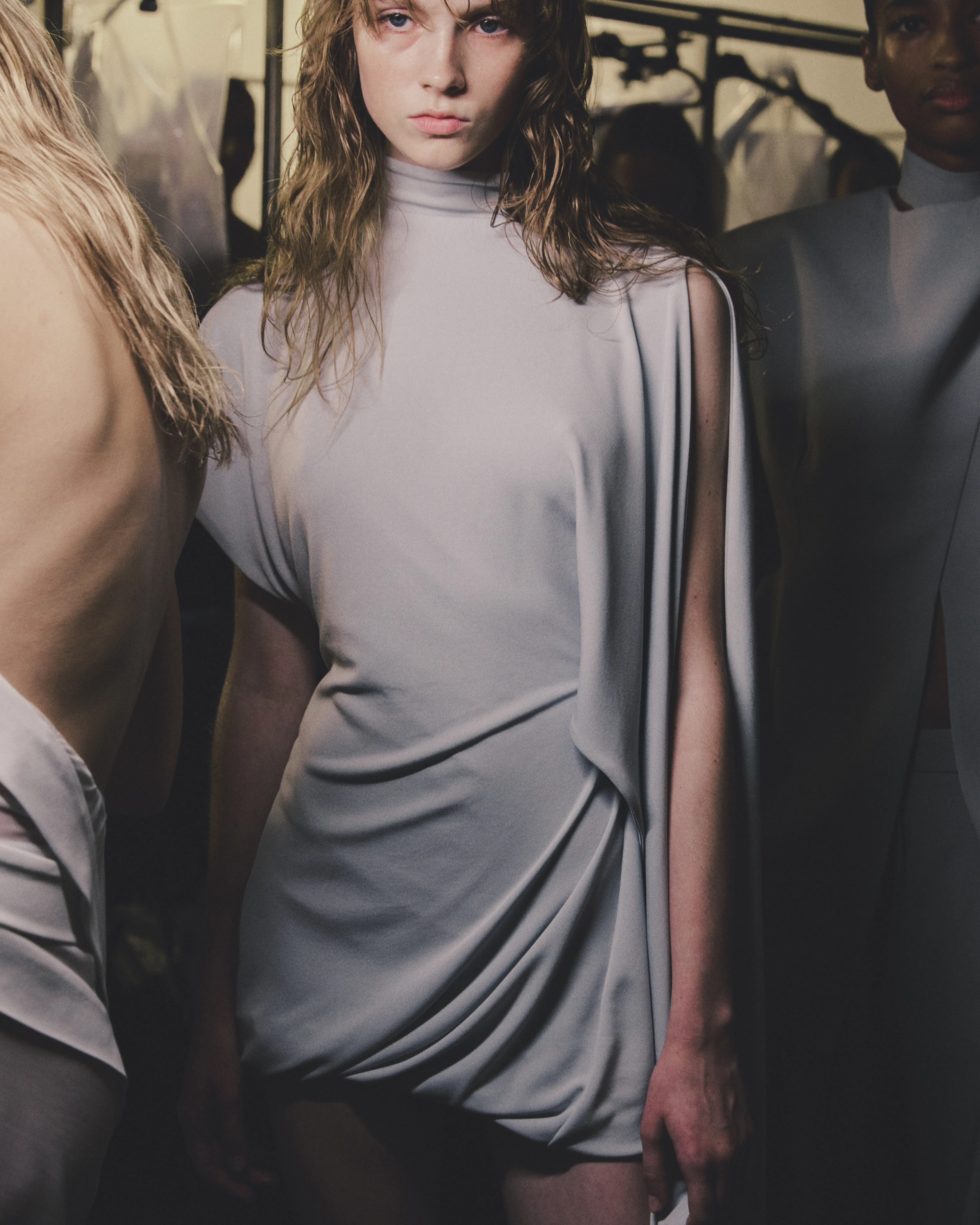 Woman in gray dress, looking. Fashion backstage with models in the dark.