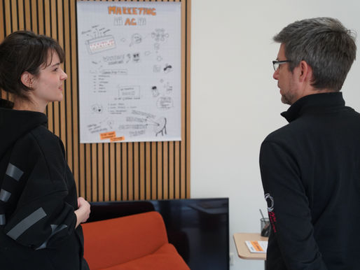 Zwei Personen stehen vor einem Plakat und unterhalten sich.