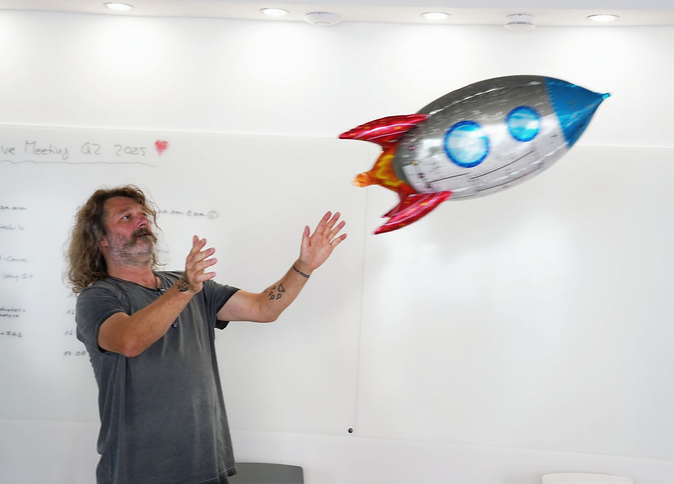 Mann in grauem T-Shirt wirft bunten Raketenballon in hellem Meeting-Raum.