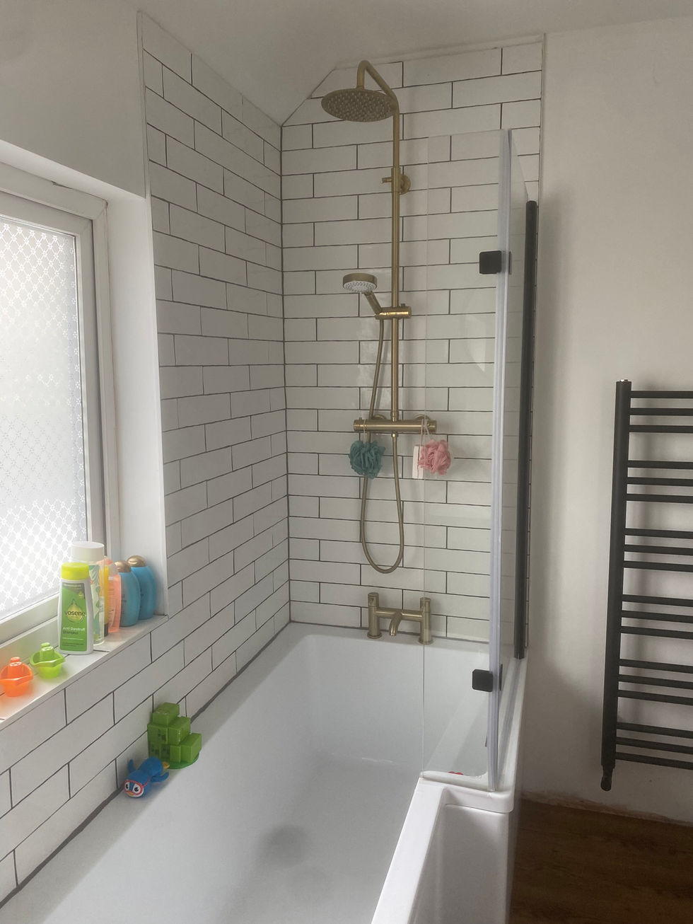 L-shaped bath with chrome effect shower unit, shower screen with black edging and a black towel rail.