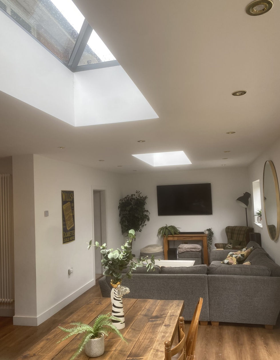 two roof lanters in a new extention with a large wooden dining table and an L-shaped sofa in the living room area