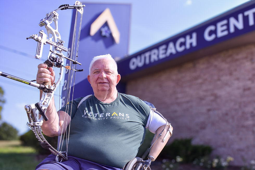 Chuck Lear holding a bow in front of the Veterans Community Project Outreach Center building