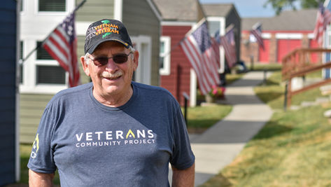 Doug smiles in front of tiny homes at Veterans Community Project