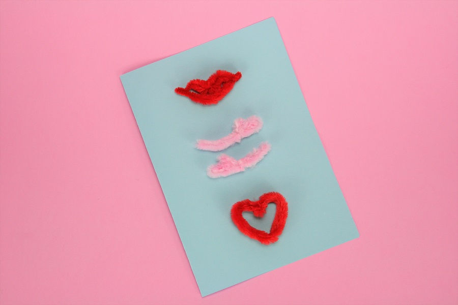 Valentinskarte mit Pfeifenputzer basteln: Pfeifenputzer Mund, Arme und Herz auf Karte kleben