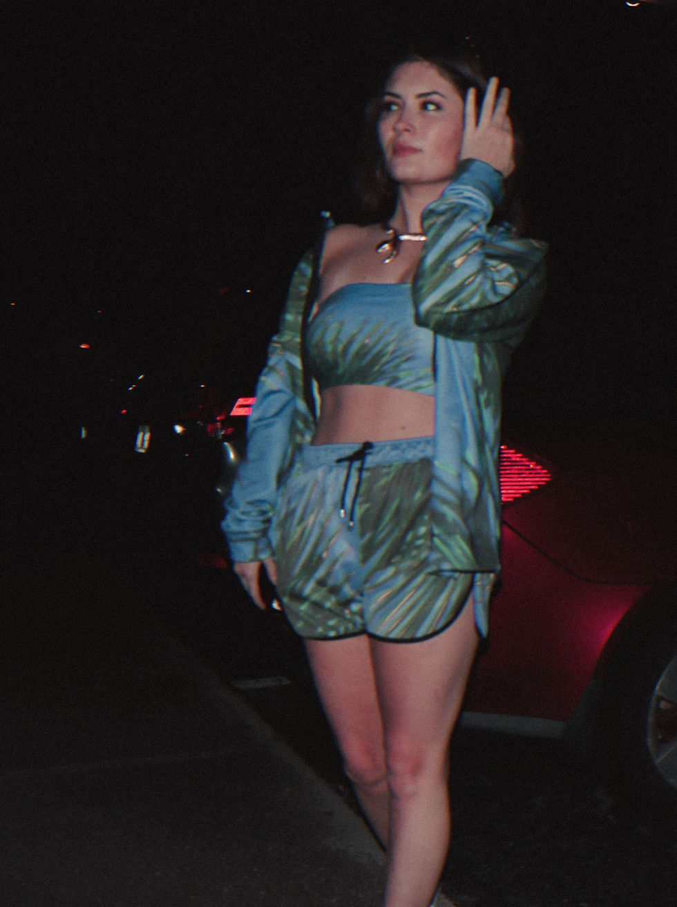 A very stylish fashionable woman in a 3 piece matching blue set - athletic shorts, a bandeau, and an athletic jacket, with palm tree details