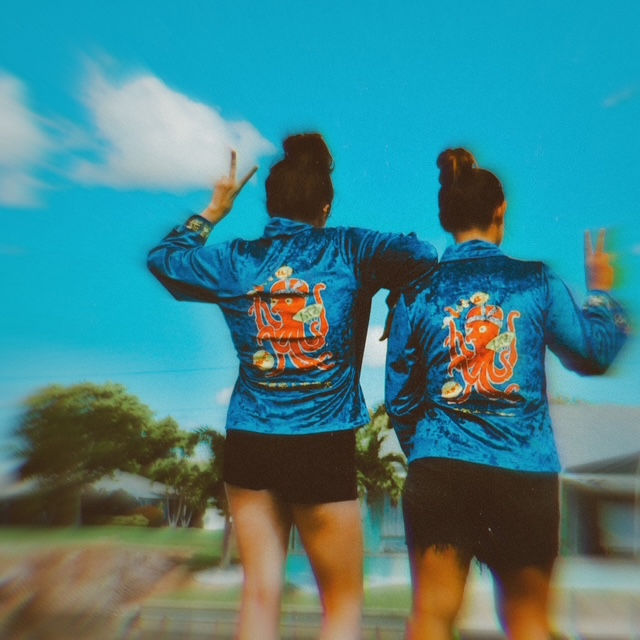 2 friends on a hazy summer day with their backs turned to the camera both wearing matching jackets with a vintage matchbook cover on them