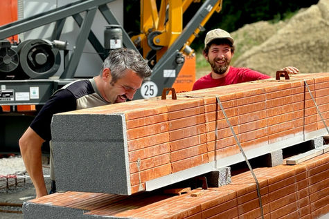 Bauleiter und Bauarbeiter auf Baustelle eines Hauses vor einer Ladung Backsteine