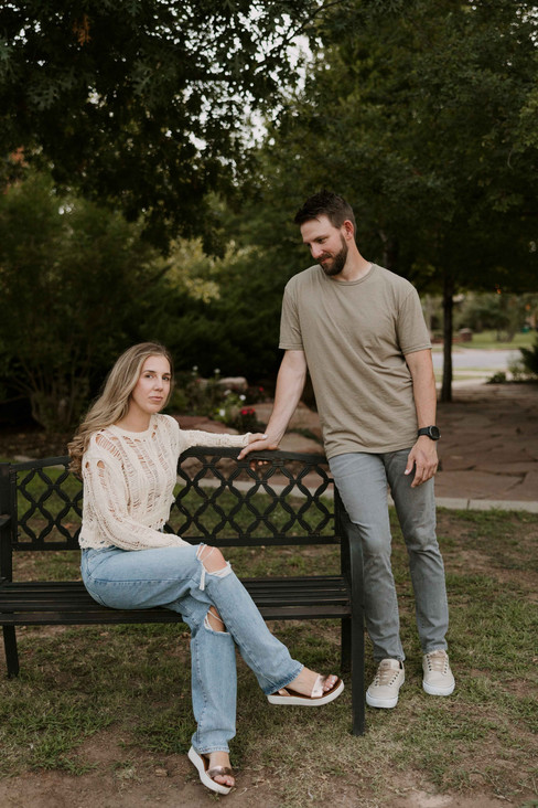 A couple sitting on a bench at a park for while showing what to wear for engagement photos.