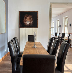 Esszimmer mit langem Holztisch, schwarzen Lederstühlen und einem Löwenbild an der Wand