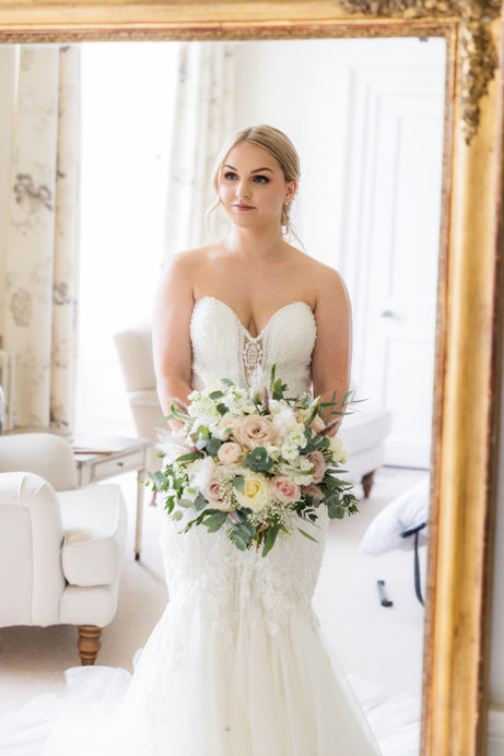bride looking into mirror holding a bouquet at Pynes house in Devon 