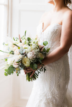 bride stood side on holding a bouquet with blush, ivory roses and pampas 