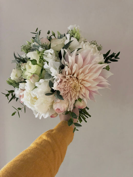 cafe au lait dahlia, ivory peony, and mixed foliages in a bouquet being held 