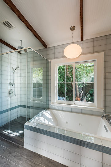 Master bathroom, glass shower, glass tiles surround the bathtub, a light fixture hangs from the vaulted ceiling