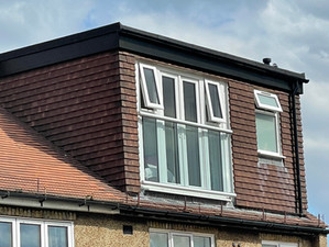 A dormer loft conversion with brown cladding, large French doors, and a Juliet balcony.

