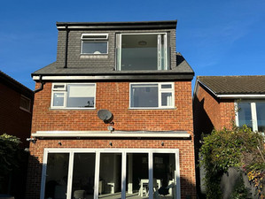 A three-story brick house with a loft conversion featuring large glass doors and a Juliet balcony.