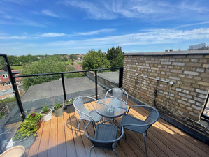 A private rooftop terrace with a wooden deck, glass railing, outdoor seating, and potted plants.