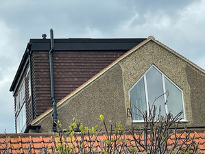 A dormer loft conversion with brown cladding, set on a pitched roof with a modern triangular window.