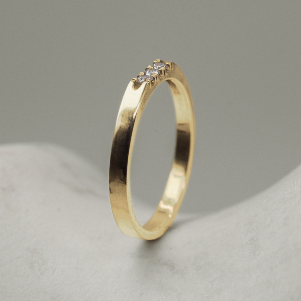 Slim 18KT yellow gold ring with three white diamonds in a fine castle setting, angled view showing polished finish