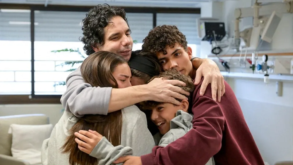 Family of five embraces warmly in a bright room with a couch and medical equipment. Emotions of joy and relief are evident.