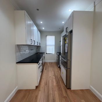 Modern galley kitchen with white cabinets, black counters, wood floor