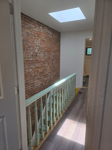 Hallway with exposed brick, skylight, green banister