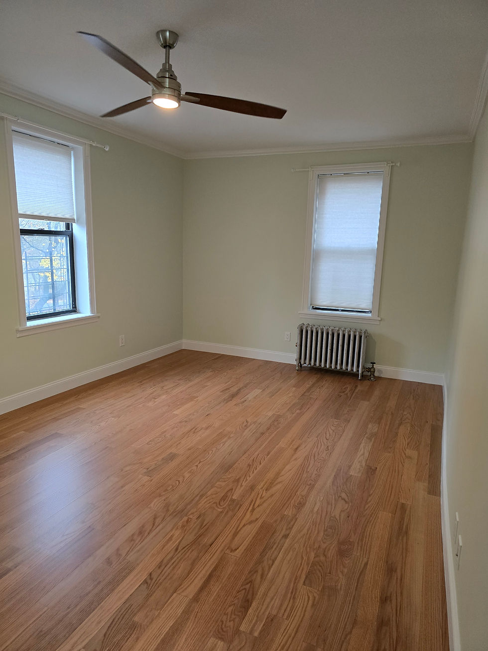 Empty room with hardwood floor, two windows, and ceiling fan
