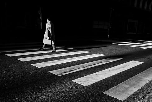 black and white picture of a man in a long coat crossing a zebra crossing