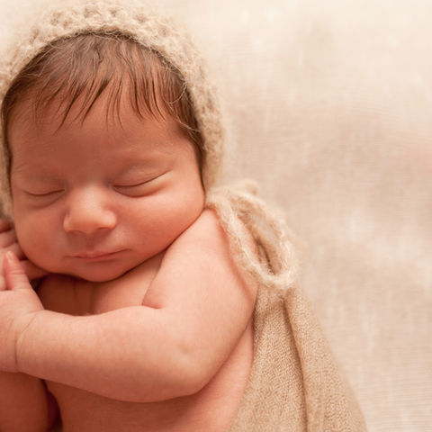 caucasian newborn in knit bonnet wrapped in muslin sleeping peacefully