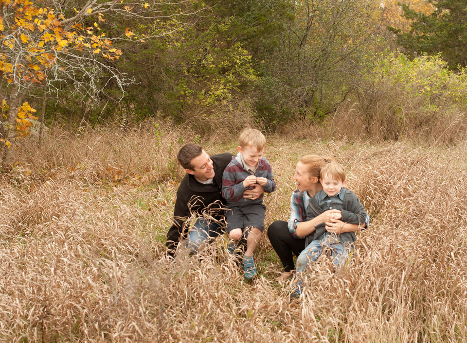happy caucasian family of four, mother, father, two sons playing as they sit in long-grasses