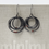 Miniatura: Los aretes colgantes concéntricos minimalistas en plata negra y chaquira roja cuelgan de la portada de un libro gris,