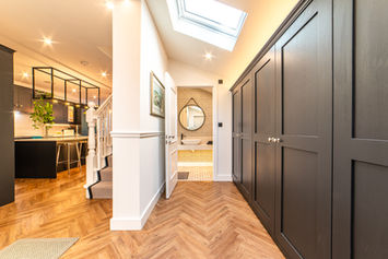 Bright kitchen walkway with skylight leading to a concealed pantry, framed by tall dark cabinetry and statement wall art.