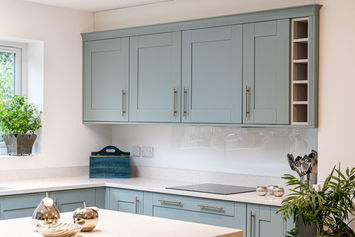 Pale blue shaker kitchen with chrome handles, central island, grey worktops, and wood-effect flooring in a bright, modern Birmingham home.