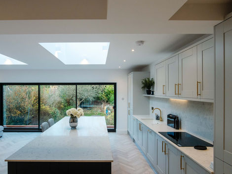 Bright kitchen with shaker cabinets, island unit, herringbone flooring and garden access, created as part of a rear extension by ProBuild360.