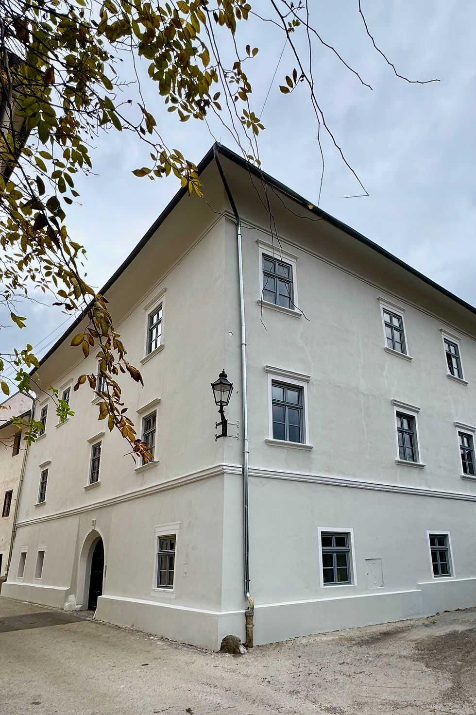 Außenansicht des historischen Maydhauses in Friesach, eines hell verputzten, dreigeschossigen Eckhauses mit grauen Fenstern und klassischer Fassadengliederung. Das Gebäude stammt aus dem 13. Jahrhundert und wurde 2023/24 behutsam revitalisiert. Es befindet sich im historischen Stadtkern innerhalb des wasserführenden Stadtgrabens und beherbergt heute das Kulturwohnzimmer Friesach – einen Ort für Austausch, Kunst und Begegnung.