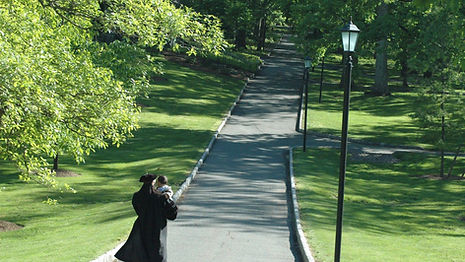 graduate in cap and gown walking college path holding infant