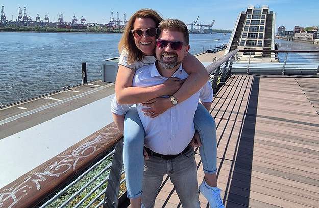 Tim nimmt Steffi Huckepack, im Hintergrund sieht man die Elbe am Hamburger Hafen