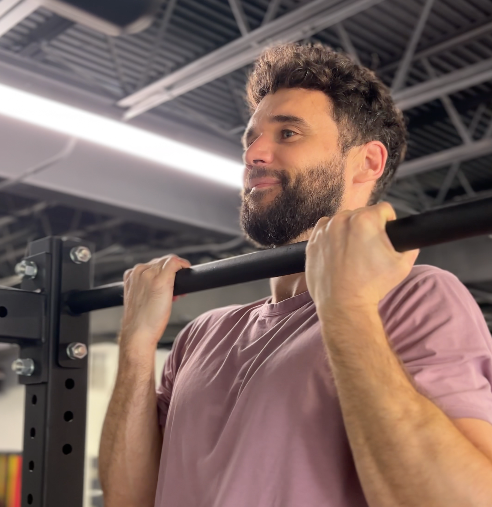 A man in a pink shirt performing chin ups in a personal training studio