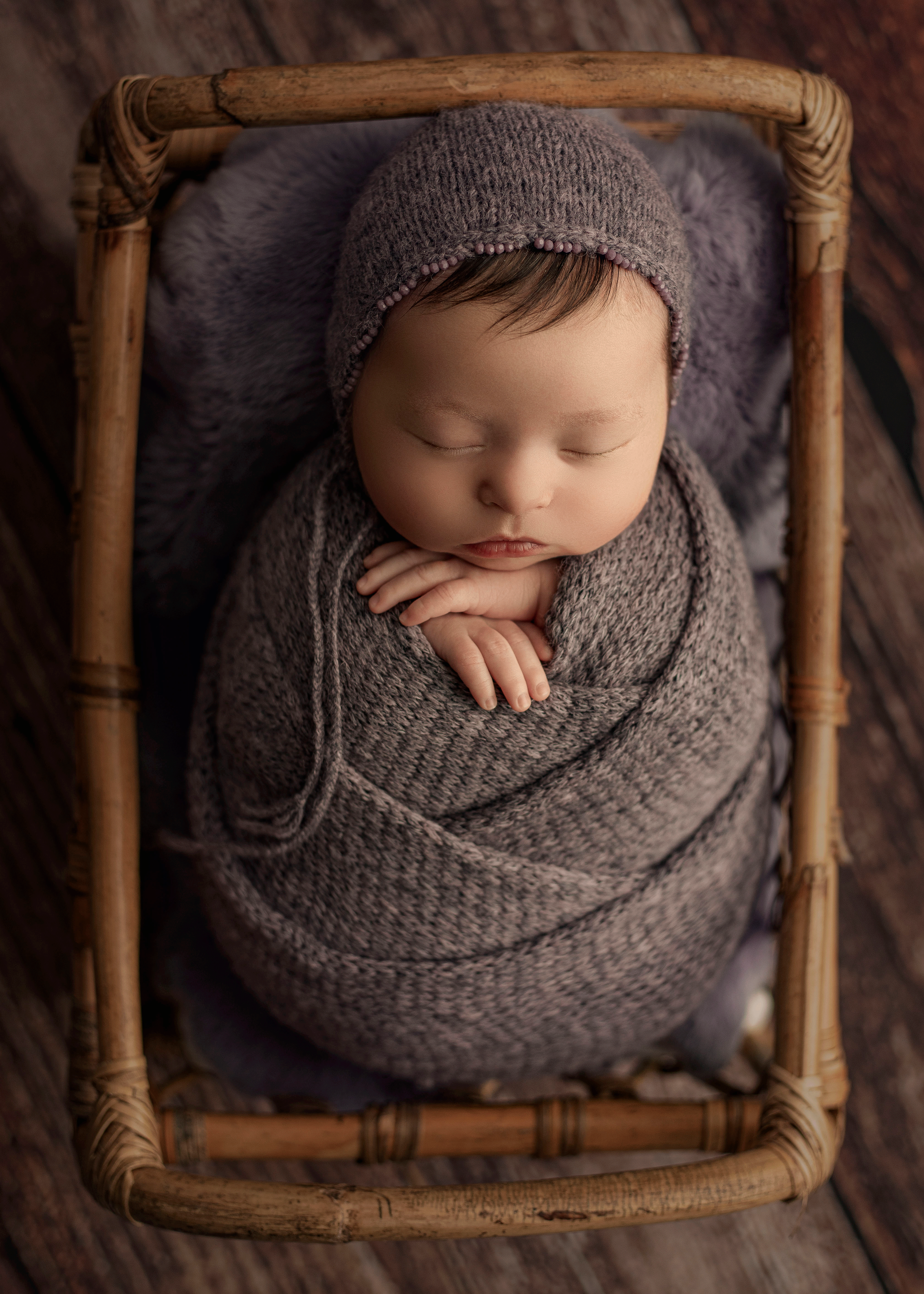 Newborn Photography of a sleeping baby girl swaddled in a purple knit wrap with a matching bonnet