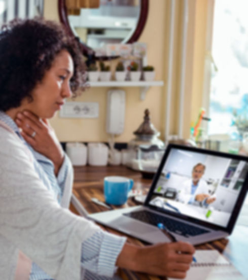 "Woman attending a virtual telehealth consultation with a doctor on a laptop while taking notes at home."