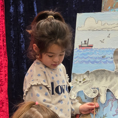 Young girl holding a paper puppet against a backdrop in theater class.