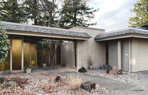 Exterior of a Barry Downs West Coast modern home in Delta, BC, with vertical siding, shingle roof, amber glass, and winter landscaping.