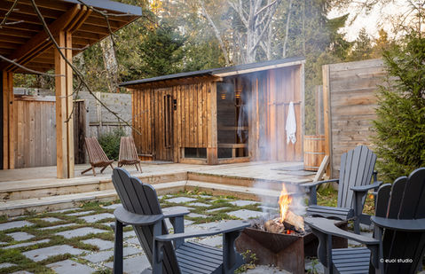 Cedar-clad sauna with outdoor fire pit, lounge chairs, and wood deck, surrounded by lush forest on the Sunshine Coast.