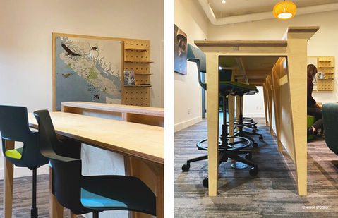 Custom plywood counter with adjustable-height seating, set against a wall map and pegboard display.