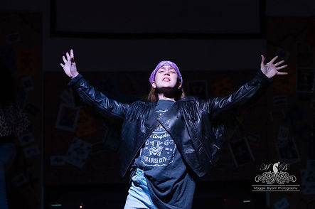 Young girl in costume singing on stage in Rock of Ages musical.